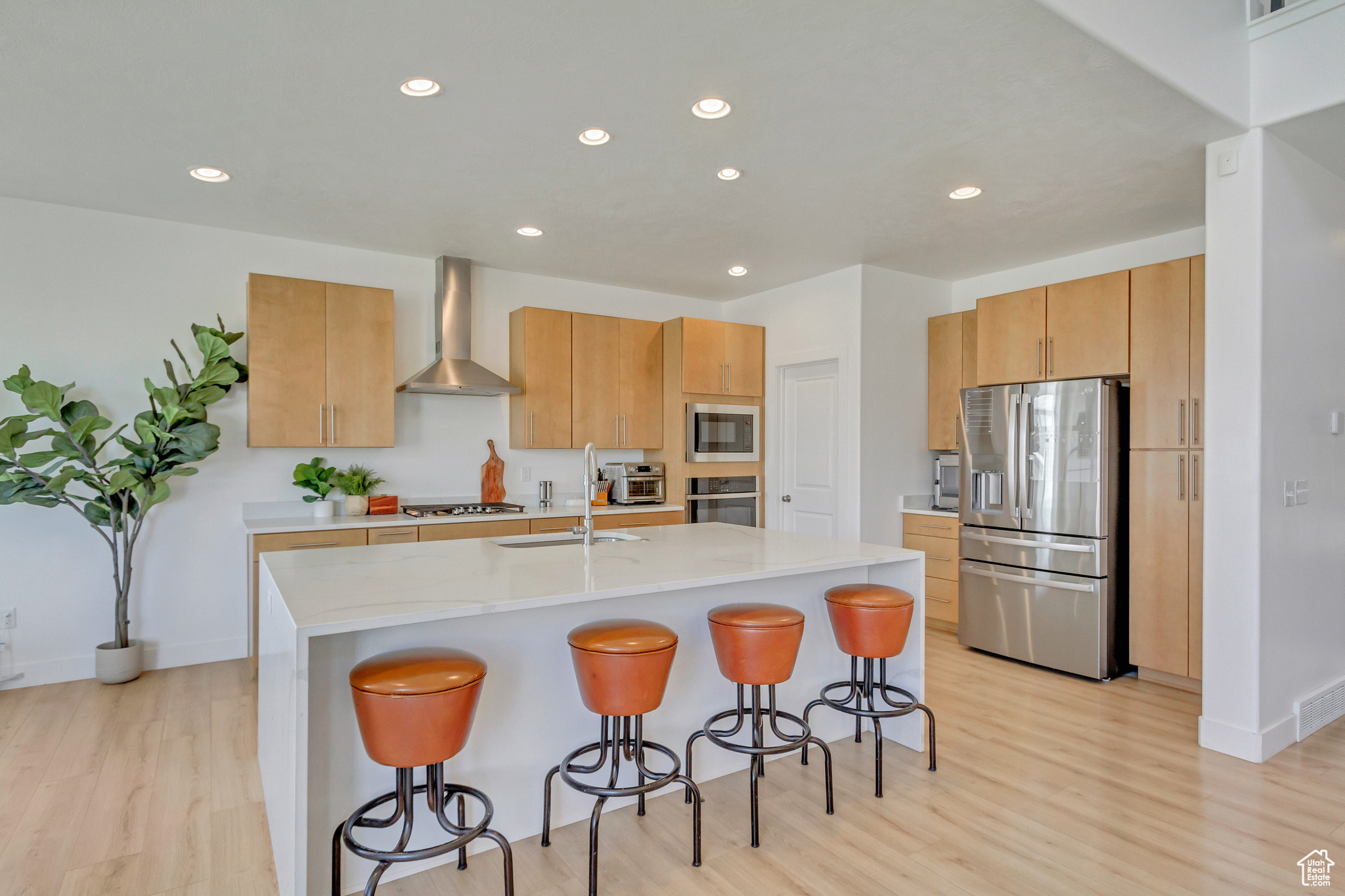 Kitchen featuring sink, a kitchen island with sink, wall chimney exhaust hood, stainless steel appliances, and light hardwood / wood-style flooring