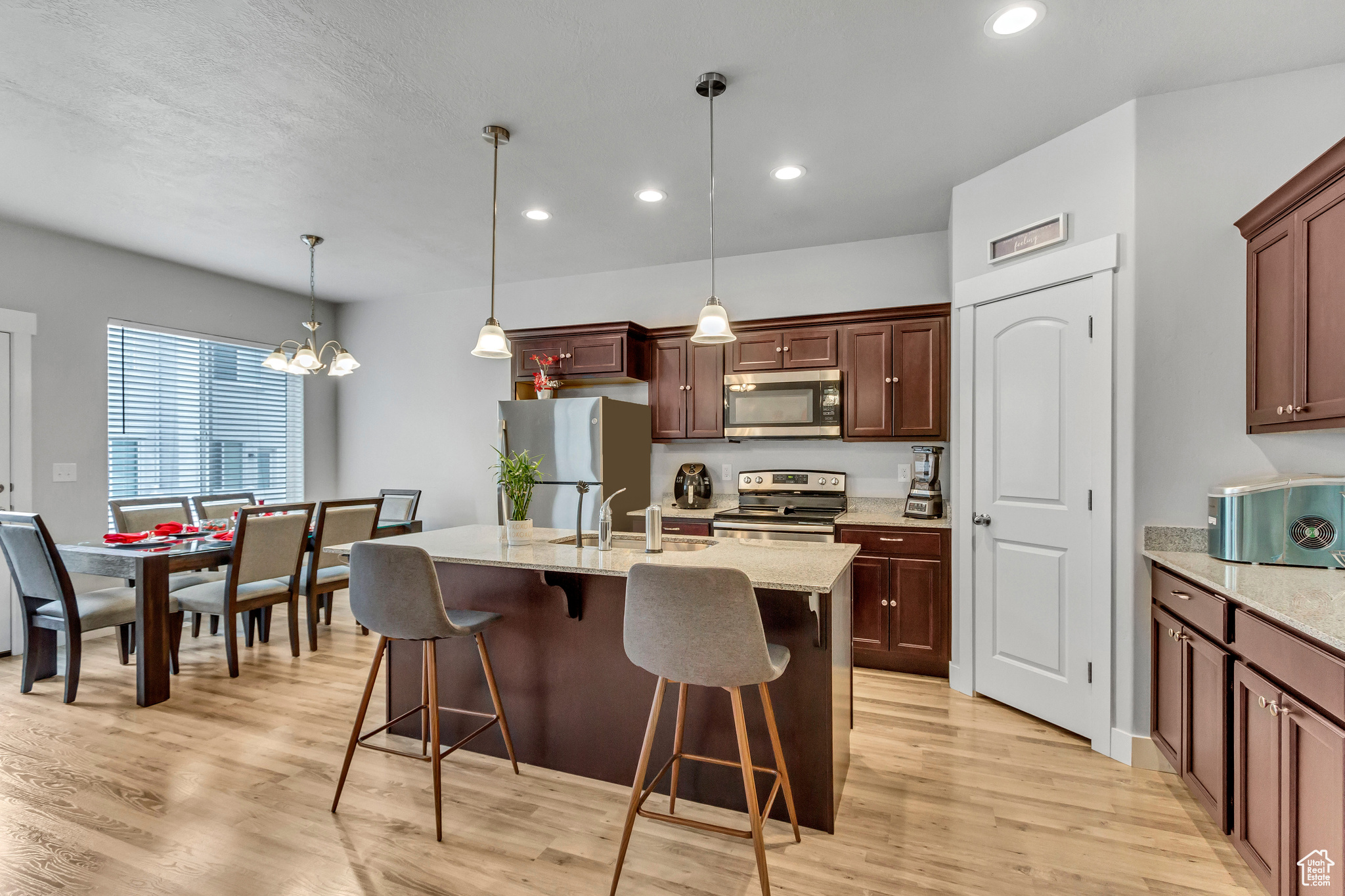 Kitchen featuring appliances with stainless steel finishes, pendant lighting, a kitchen bar, a kitchen island with sink, and light hardwood / wood-style floors