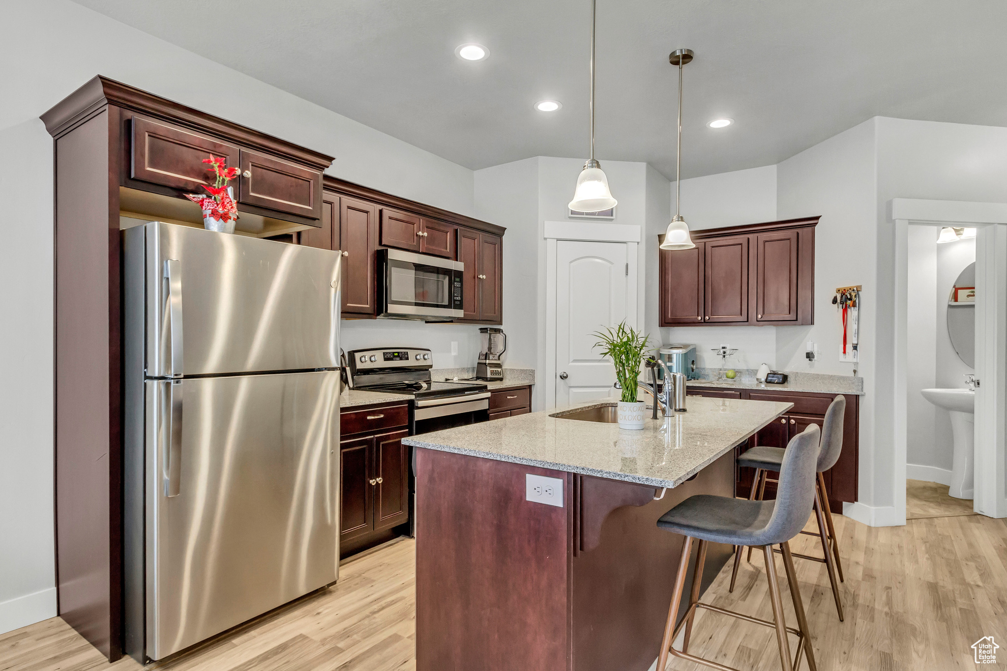 Kitchen featuring a breakfast bar, an island with sink, sink, stainless steel appliances, and light stone countertops