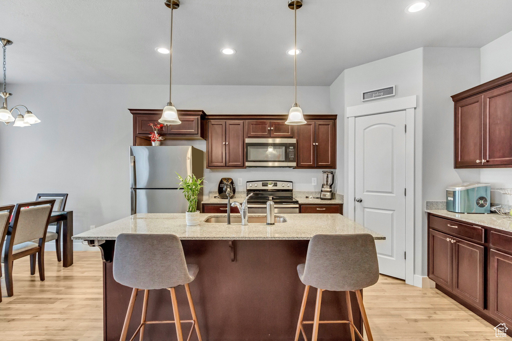 Kitchen featuring stainless steel appliances, decorative light fixtures, and an island with sink