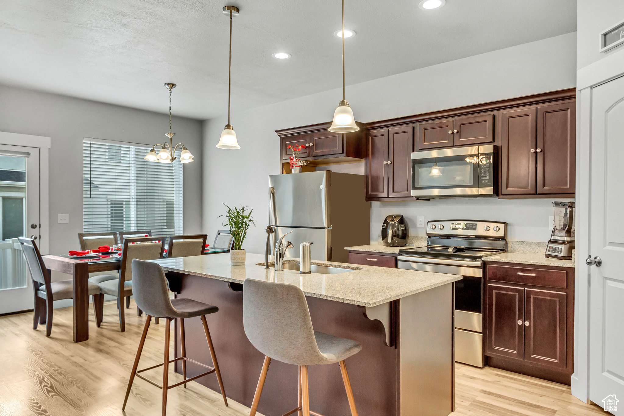 Kitchen featuring sink, hanging light fixtures, light wood-type flooring, appliances with stainless steel finishes, and a kitchen island with sink