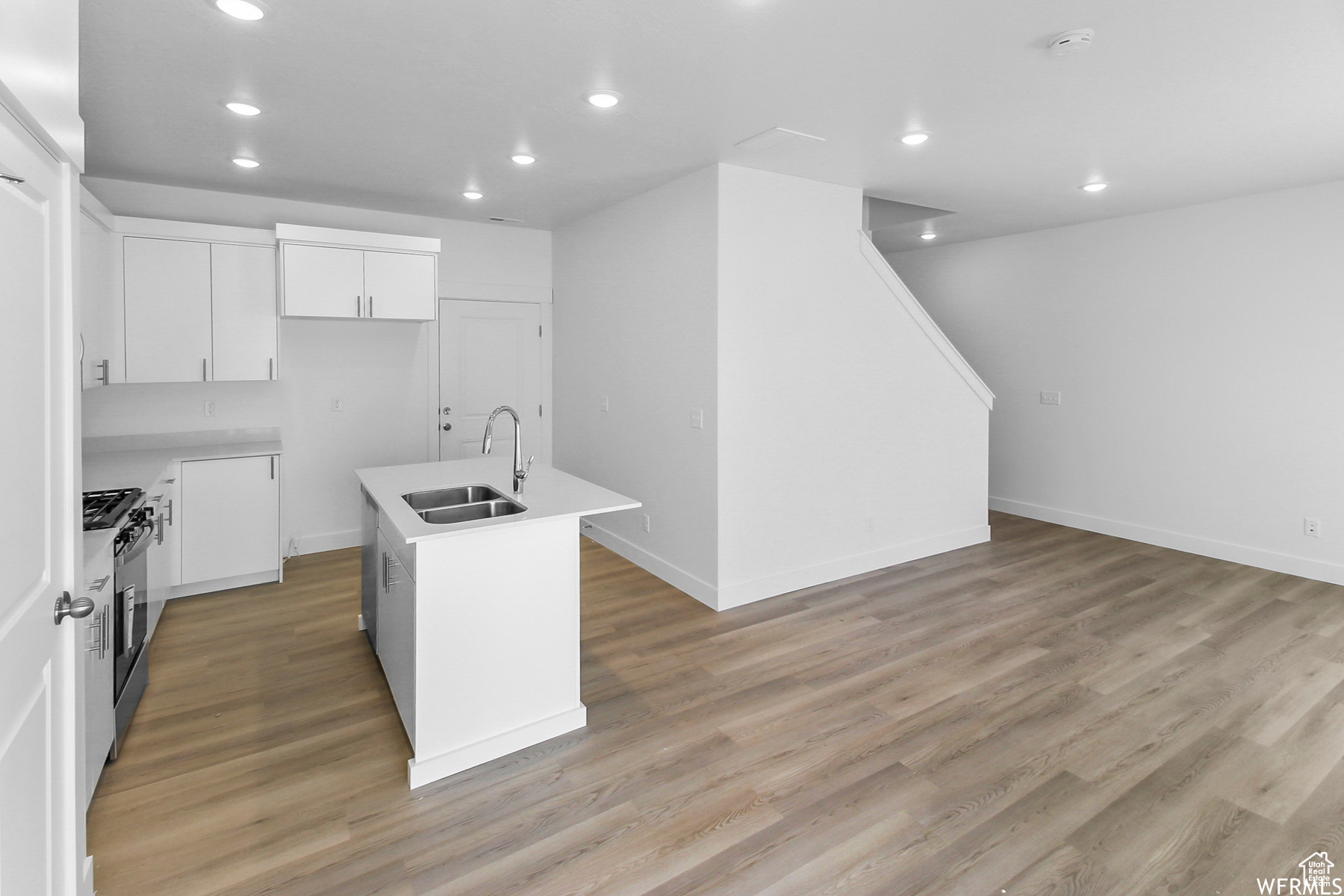 Kitchen featuring white cabinetry, stainless steel appliances, a center island with sink, and light wood-type flooring