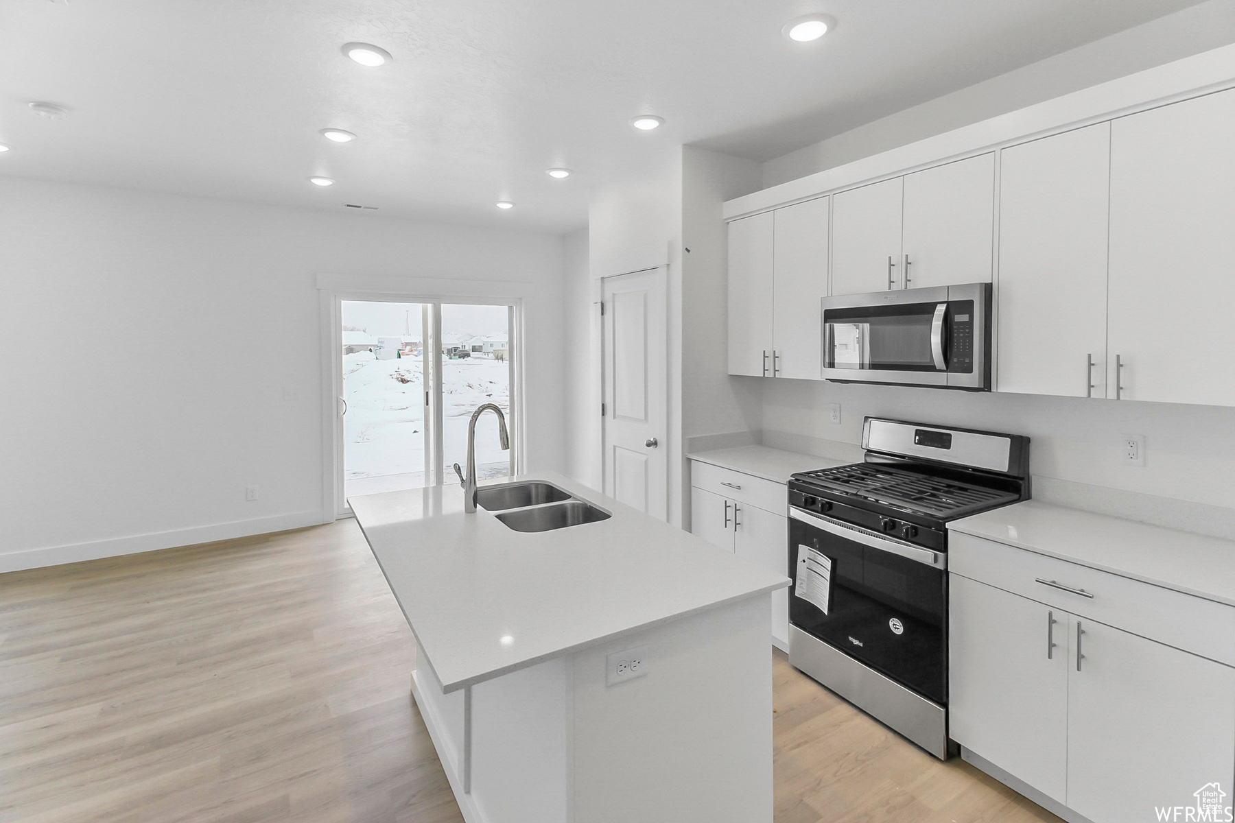 Kitchen with stainless steel appliances, an island with sink, sink, and white cabinets