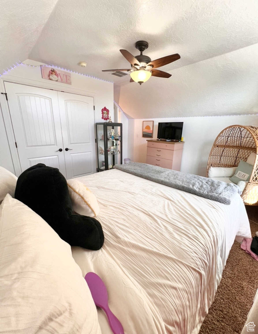 Carpeted bedroom with ceiling fan, vaulted ceiling, a closet, and a textured ceiling