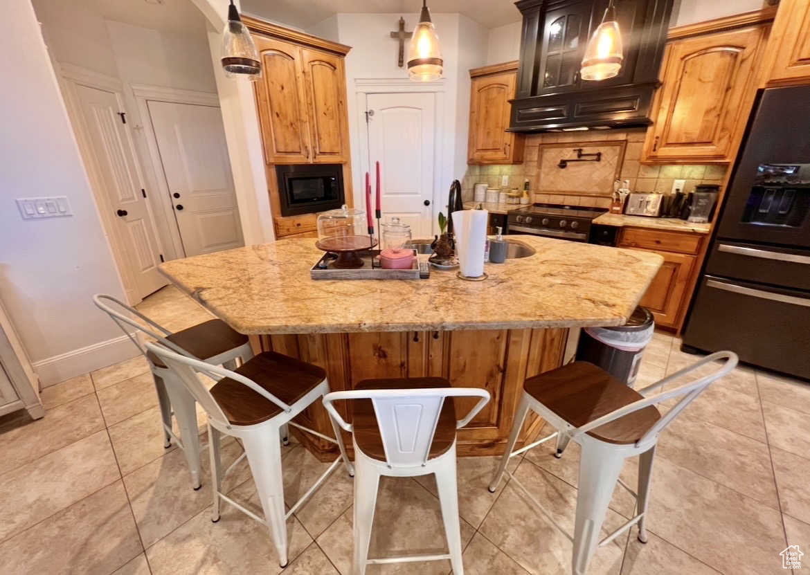 Kitchen featuring a kitchen breakfast bar, an island with sink, custom exhaust hood, and black appliances