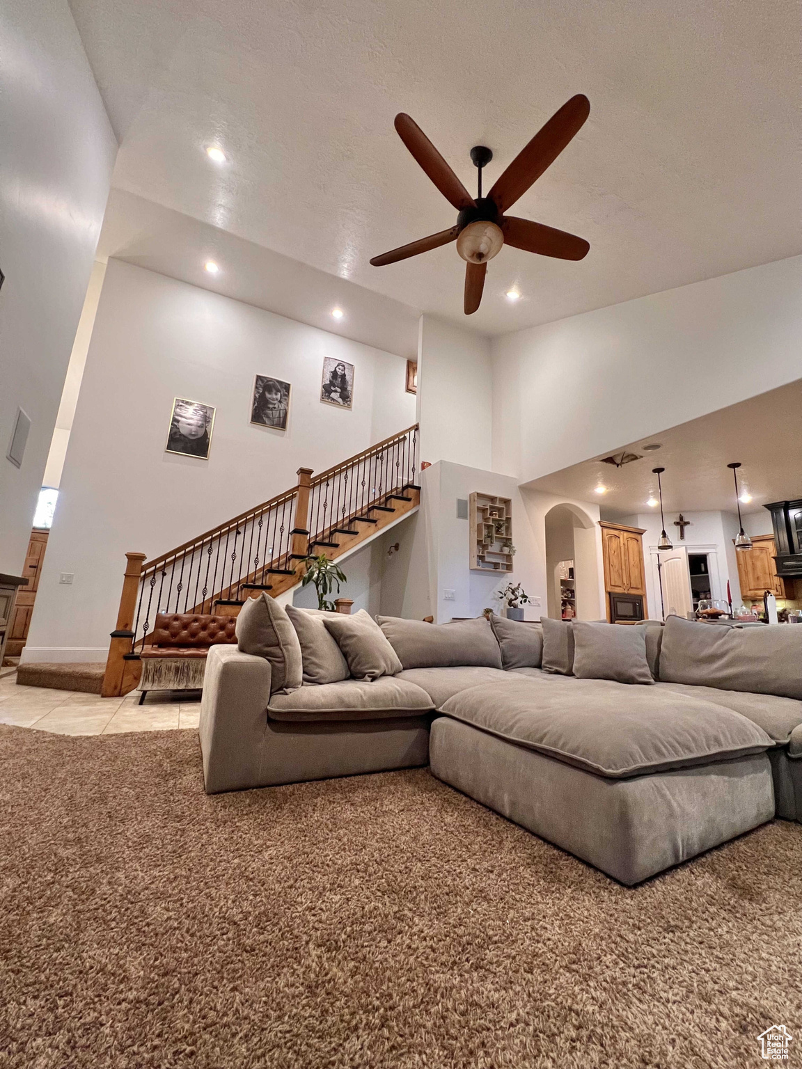 Carpeted living room with ceiling fan and high vaulted ceiling