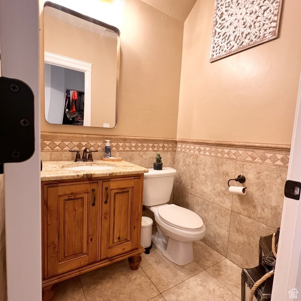 Bathroom featuring tile patterned flooring, vanity, tile walls, and toilet