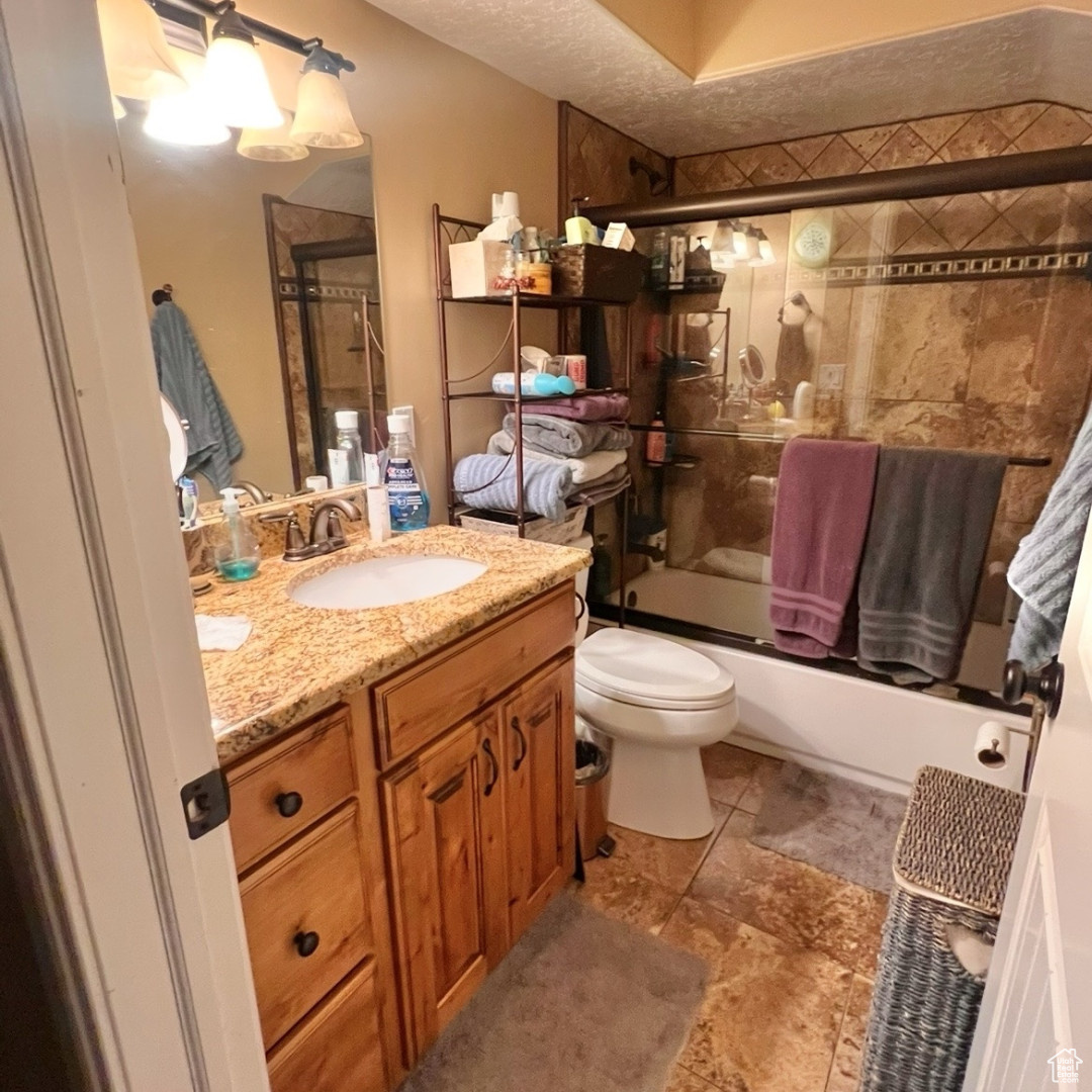 Full bathroom with vanity, toilet, shower / bath combination with glass door, and a textured ceiling