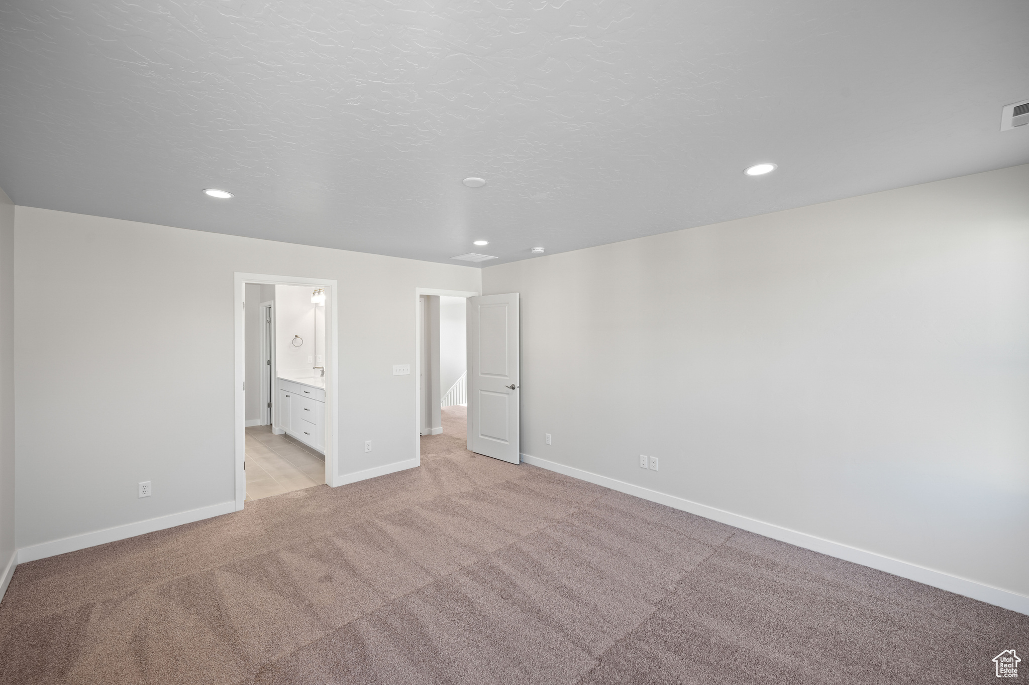 Unfurnished bedroom with ensuite bath, light colored carpet, and a textured ceiling