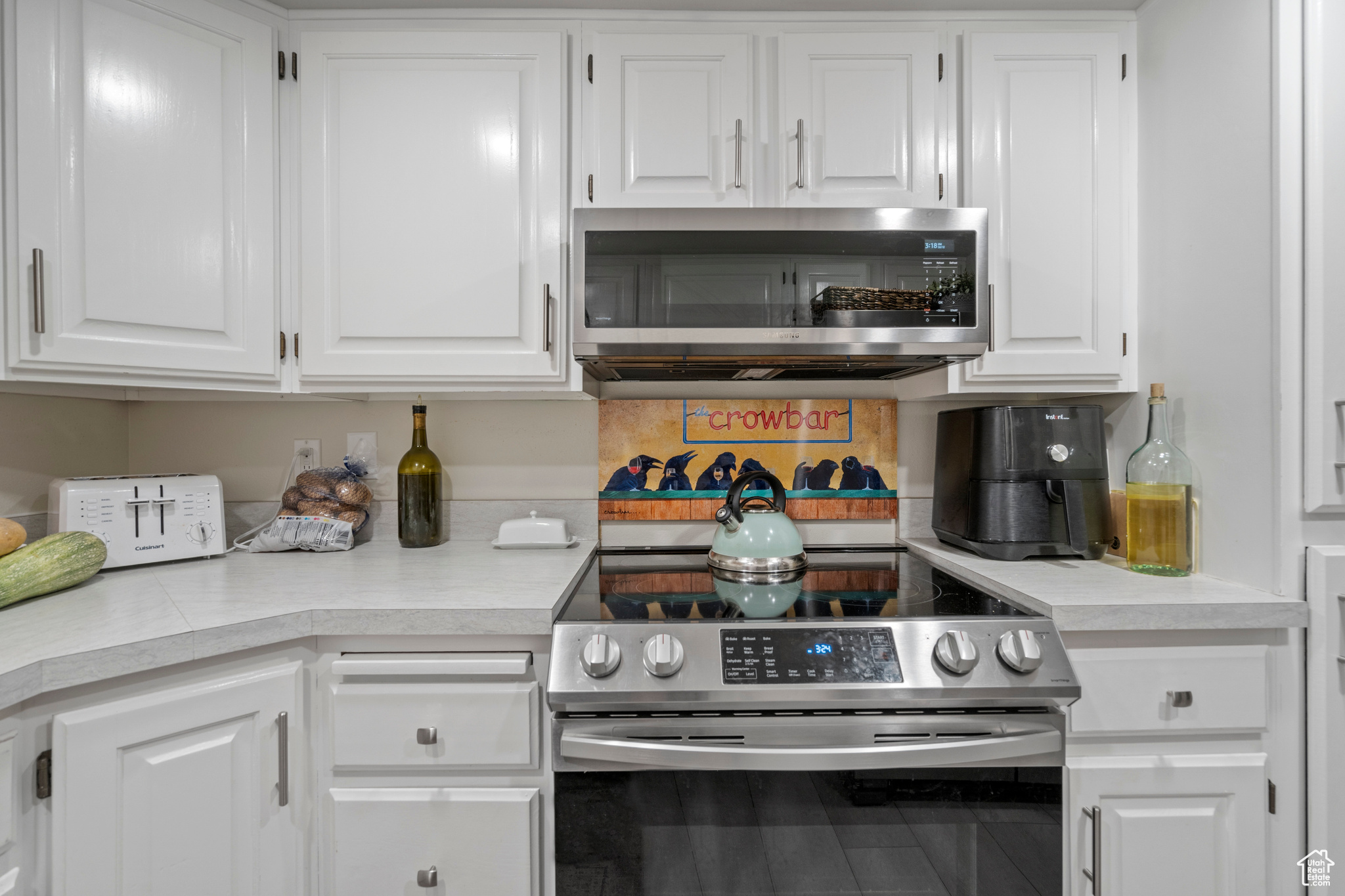 Kitchen with stainless steel appliances, decorative backsplash, and white cabinets