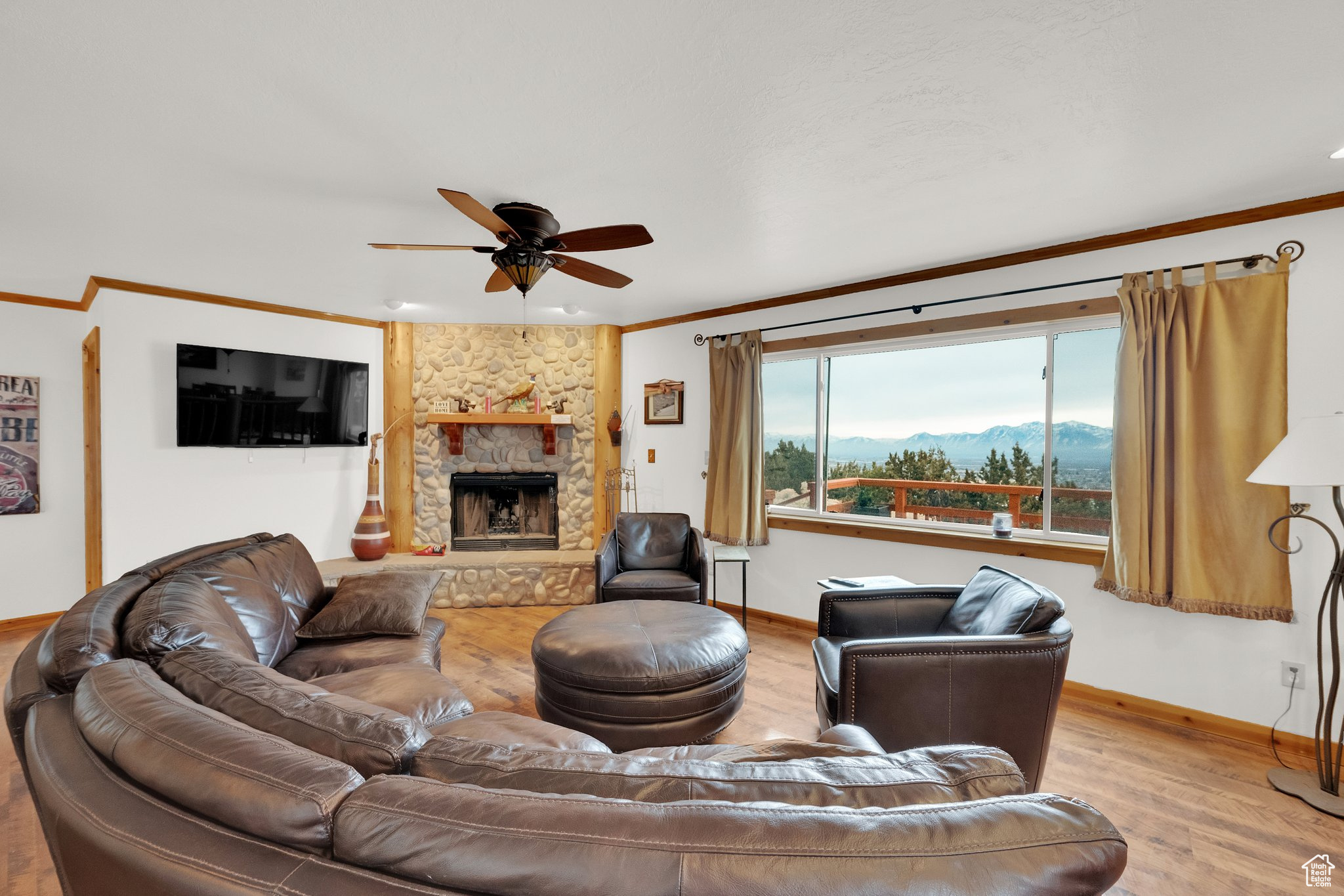 Living room featuring crown molding, ceiling fan, a stone fireplace, and light hardwood / wood-style floors