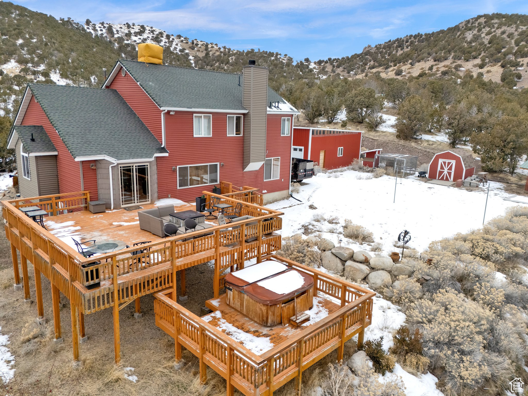 Snow covered rear of property featuring a shed, a hot tub, and a deck with mountain view