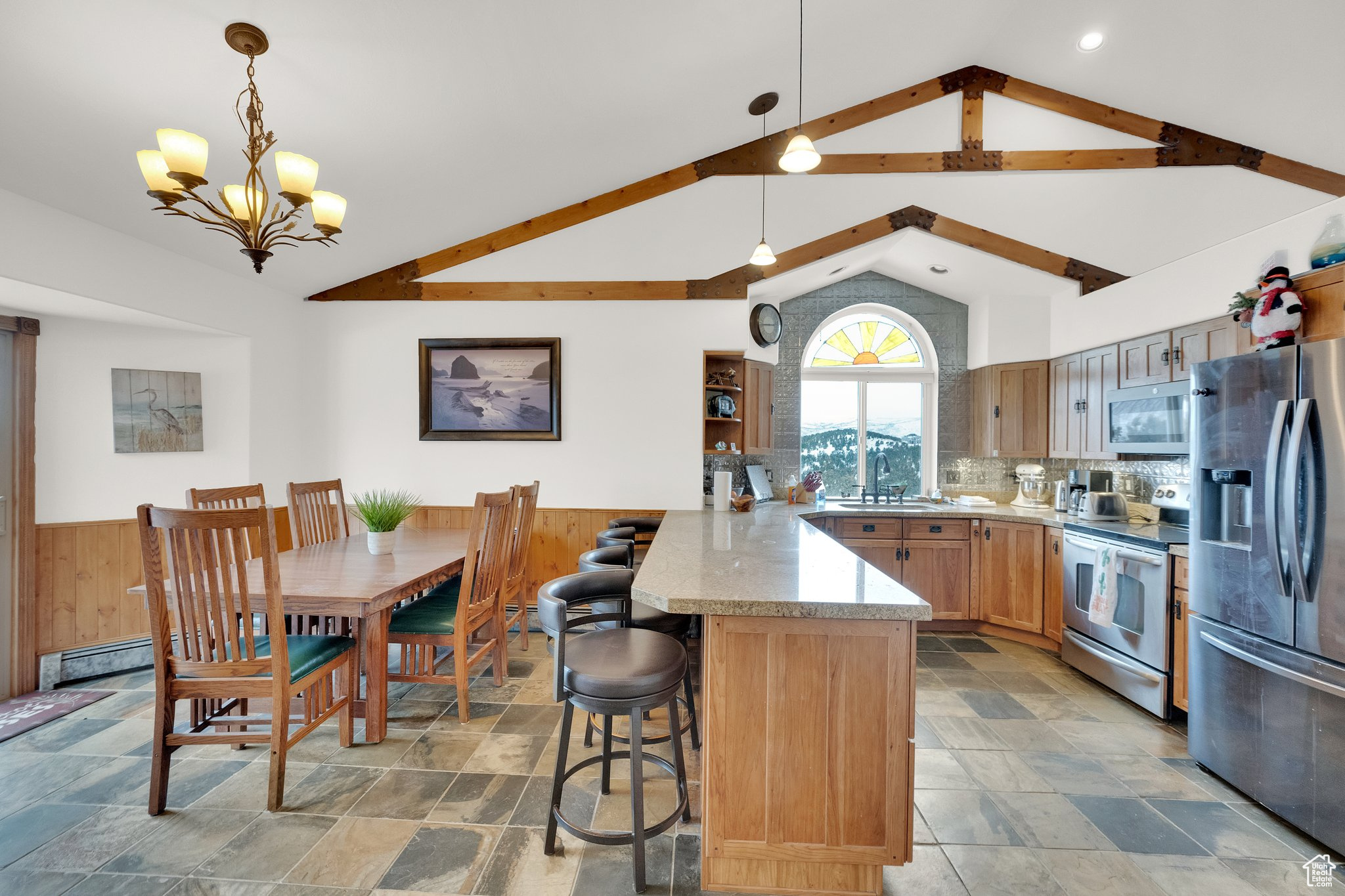 Kitchen with stainless steel appliances, vaulted ceiling, hanging light fixtures, and wood walls