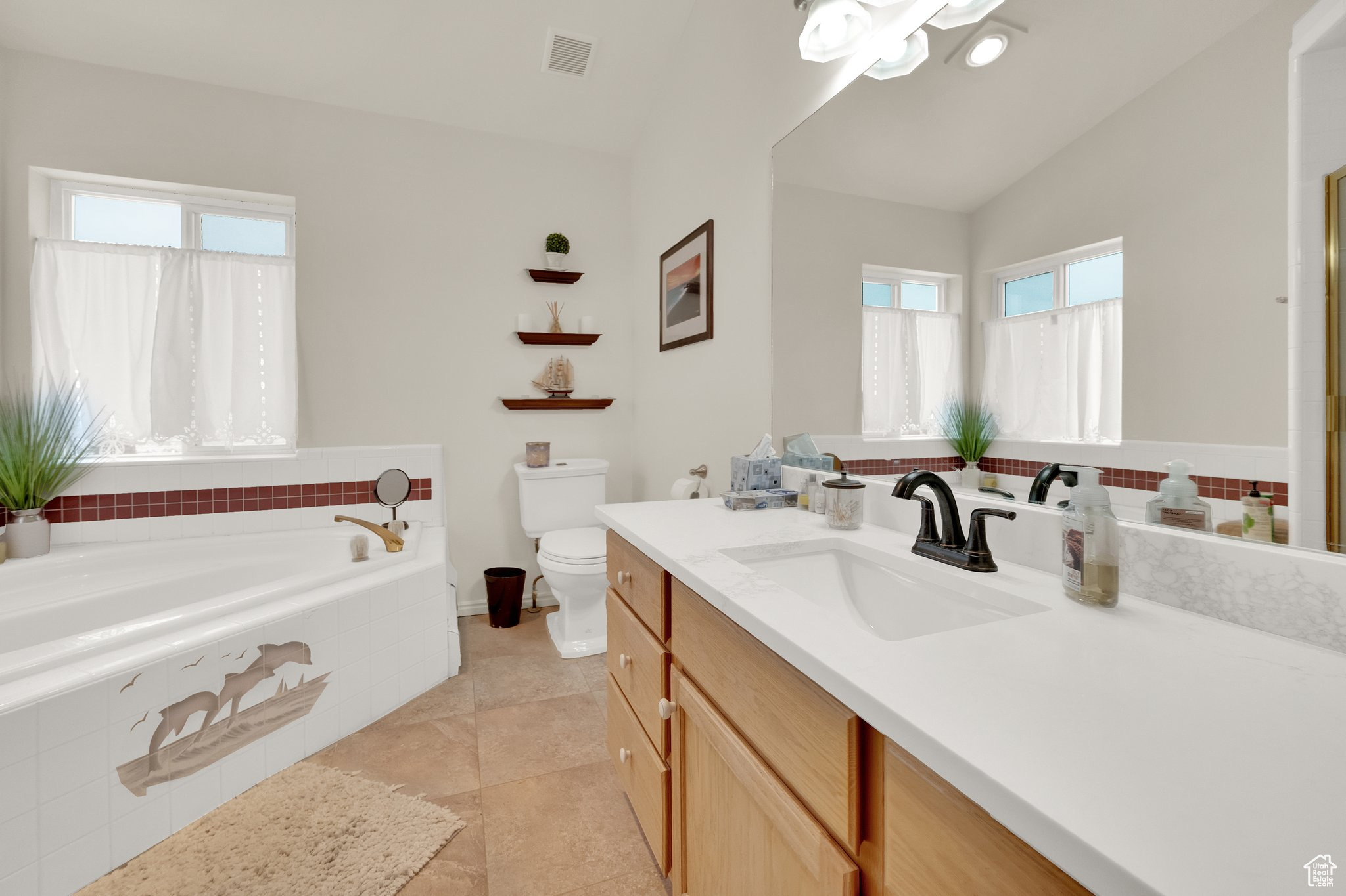 Bathroom with lofted ceiling, tiled tub, tile patterned flooring, vanity, and toilet