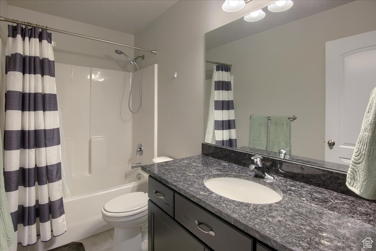 Full bathroom with tile patterned floors, vanity, toilet, and shower / bath combo with shower curtain