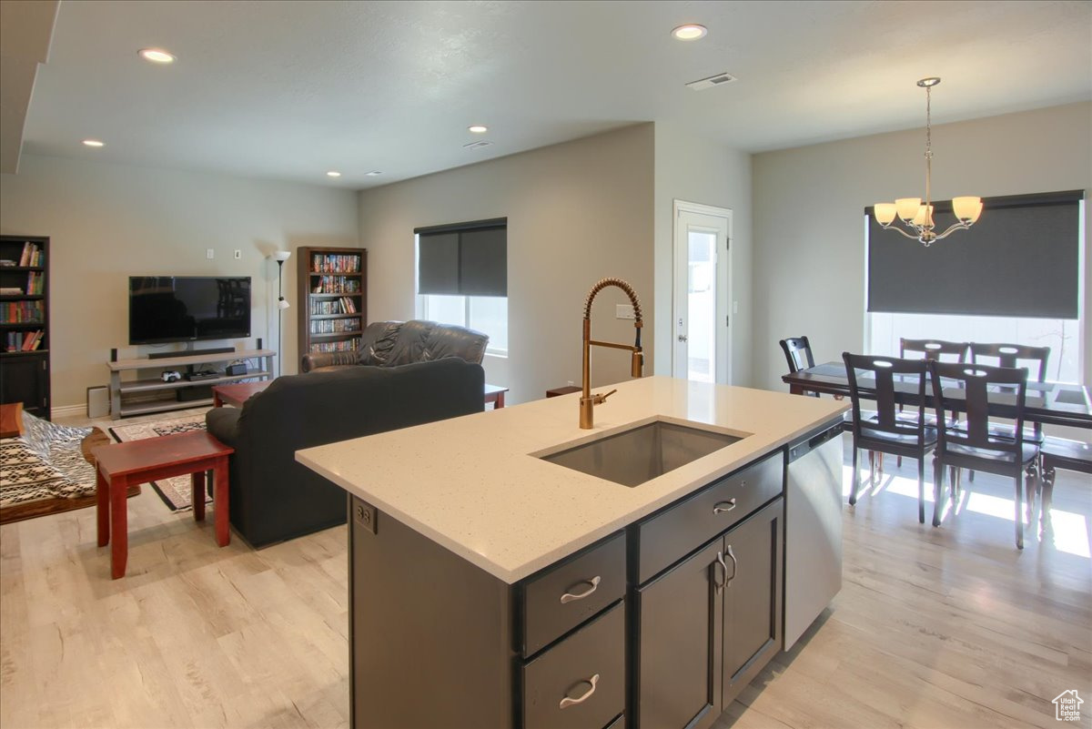 Kitchen featuring sink, dishwasher, a center island with sink, decorative light fixtures, and light wood-type flooring