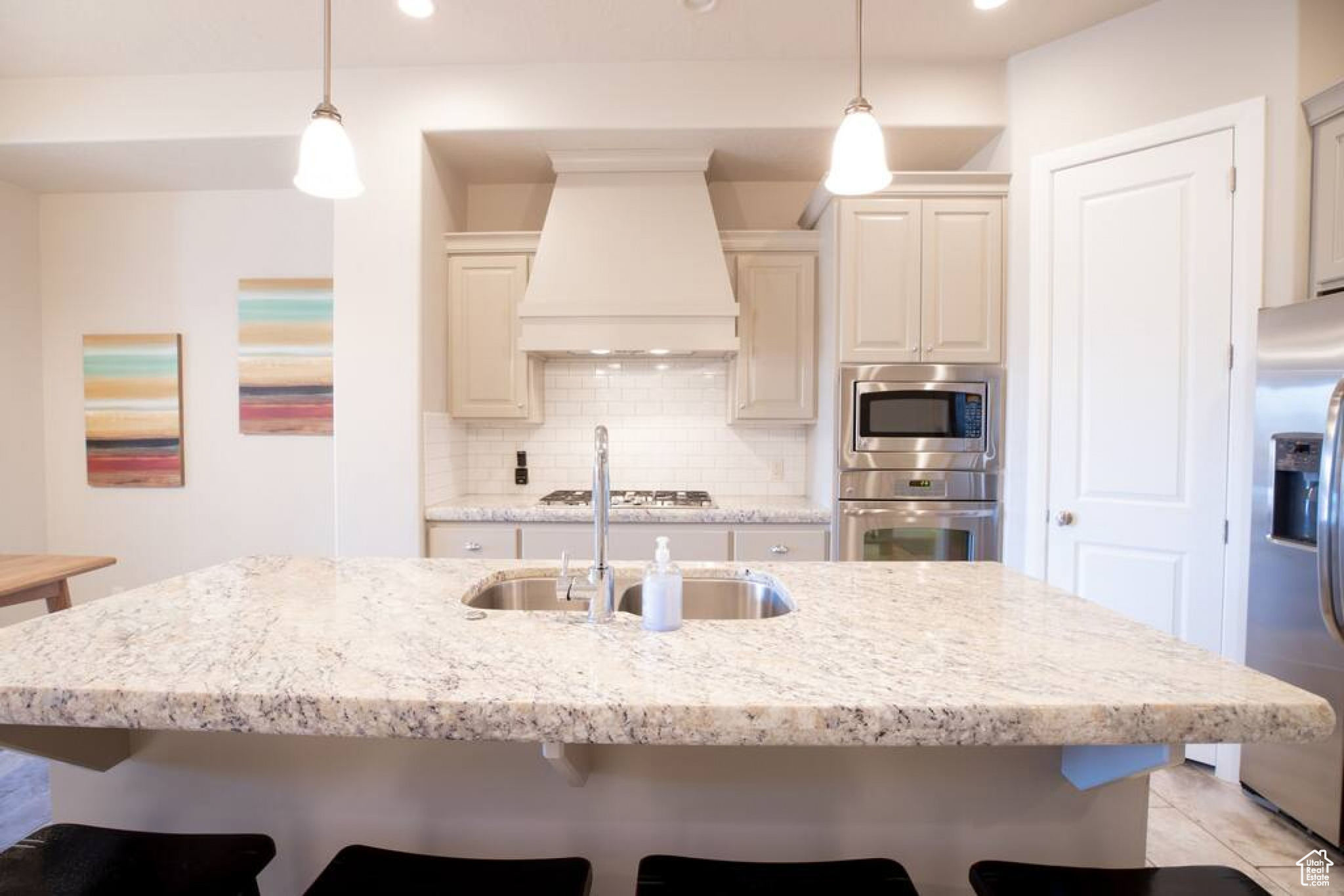 Kitchen featuring premium range hood, appliances with stainless steel finishes, decorative light fixtures, and cream cabinetry