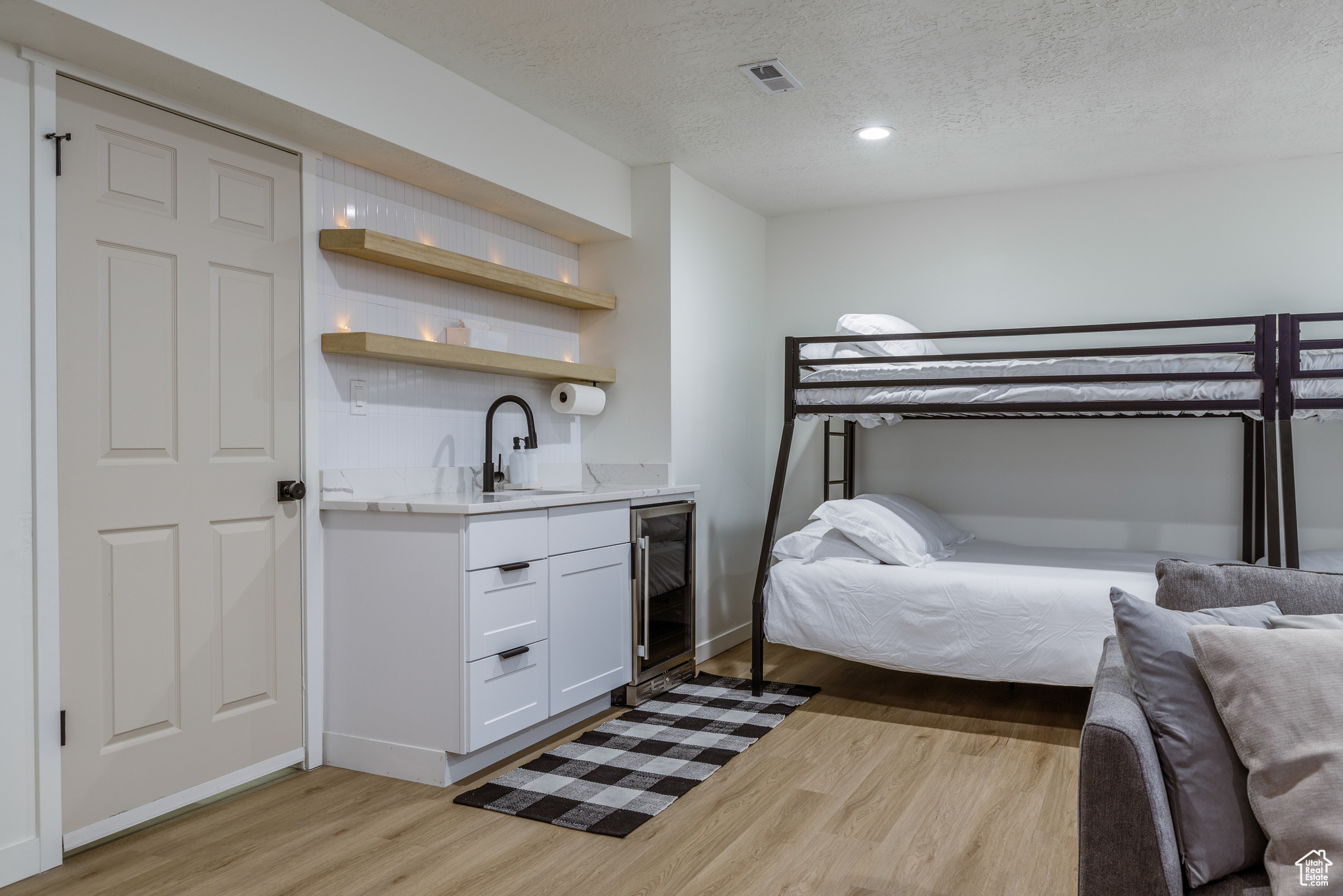 Bedroom with wet bar, beverage cooler, a textured ceiling, and light hardwood / wood-style flooring