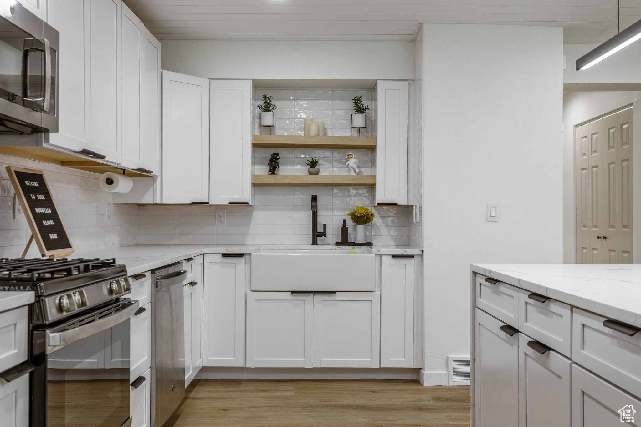 Kitchen featuring sink, appliances with stainless steel finishes, tasteful backsplash, light stone countertops, and white cabinets