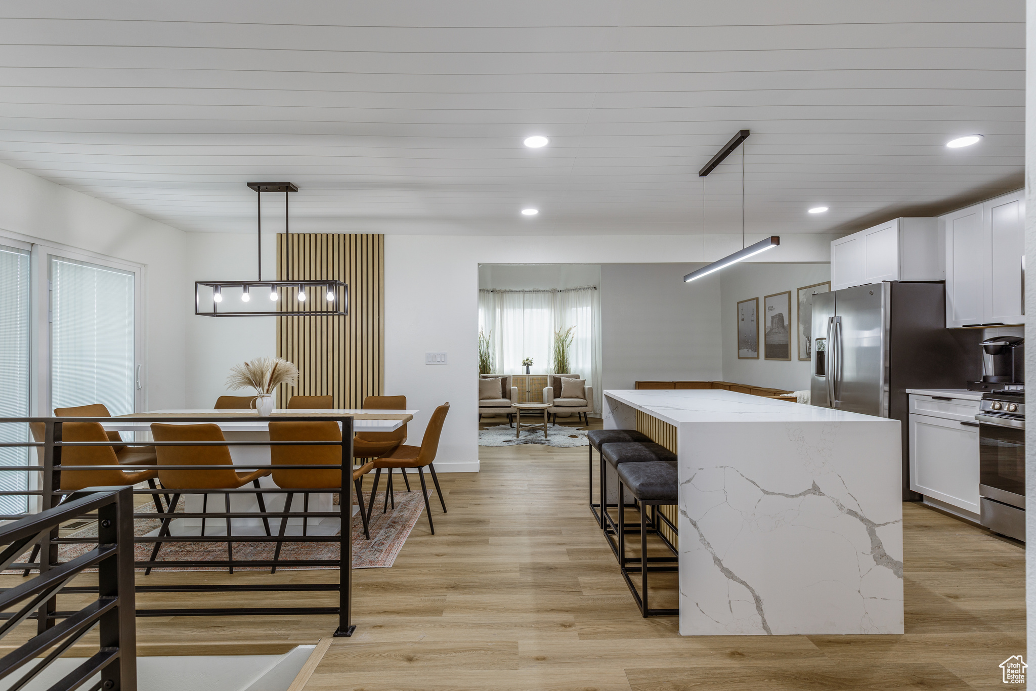 Kitchen with light stone counters, stainless steel range with gas cooktop, a kitchen island, pendant lighting, and white cabinets