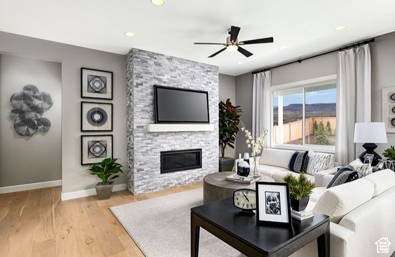 Living room featuring a stone fireplace, ceiling fan, and light wood-type flooring