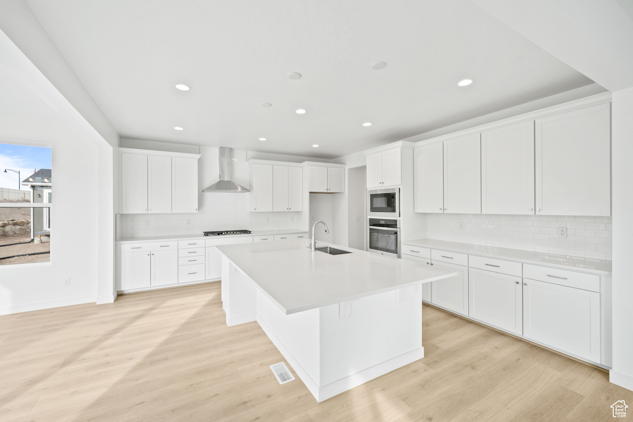 Kitchen with a center island with sink, wall chimney range hood, sink, gas stovetop, and white cabinetry