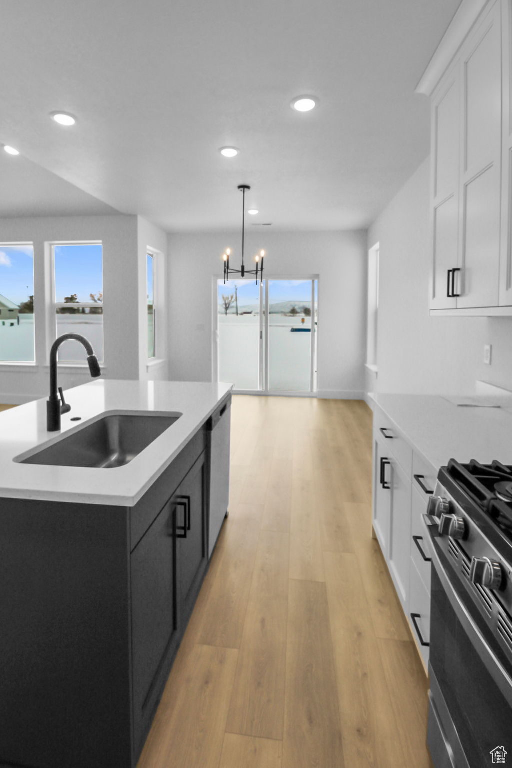 Kitchen with sink, white cabinetry, range with gas stovetop, a center island with sink, and decorative light fixtures