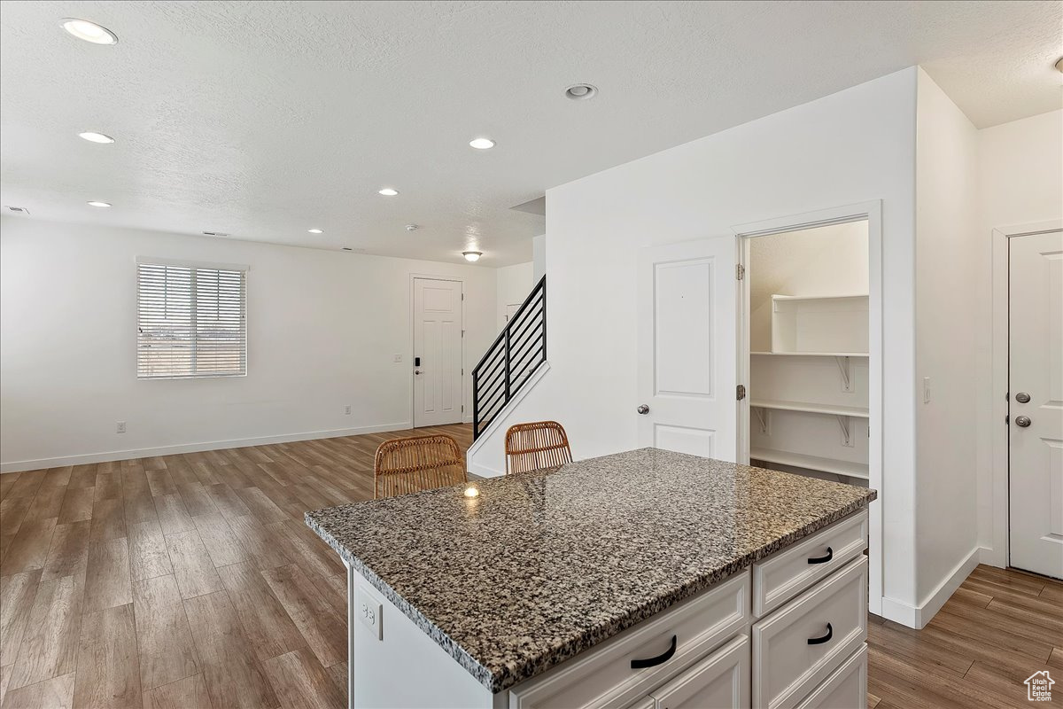 Kitchen with light hardwood / wood-style flooring, stone counters, a kitchen island, white cabinets, and a textured ceiling