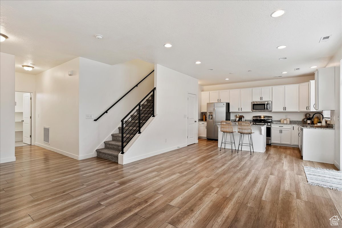 Kitchen featuring light hardwood / wood-style flooring, a kitchen island, stainless steel appliances, white cabinets, and a kitchen bar