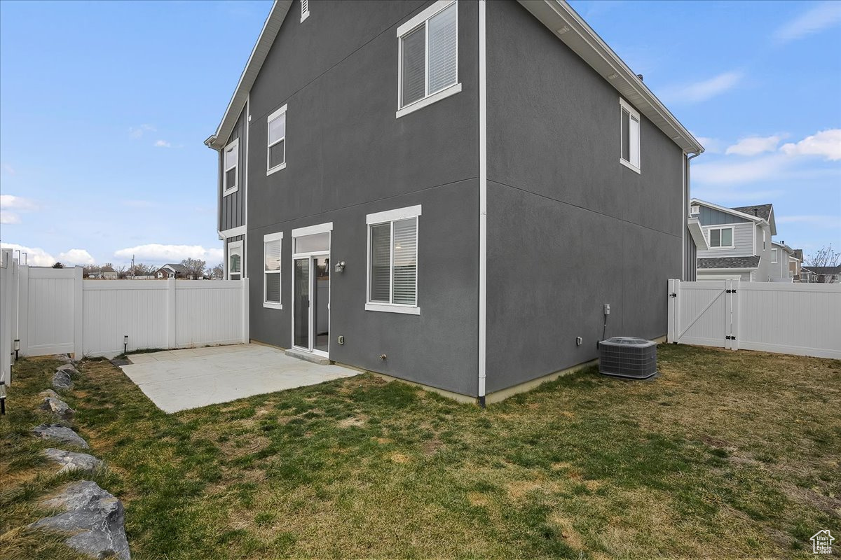 Rear view of house with central AC unit, a patio area, and a lawn