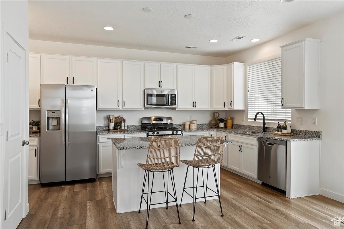 Kitchen featuring sink, white cabinetry, a center island, appliances with stainless steel finishes, and light stone countertops