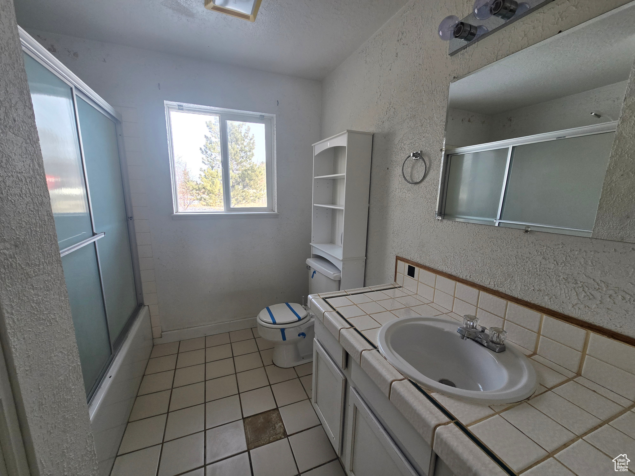 Full bathroom featuring tile patterned flooring, bath / shower combo with glass door, vanity, a textured ceiling, and toilet