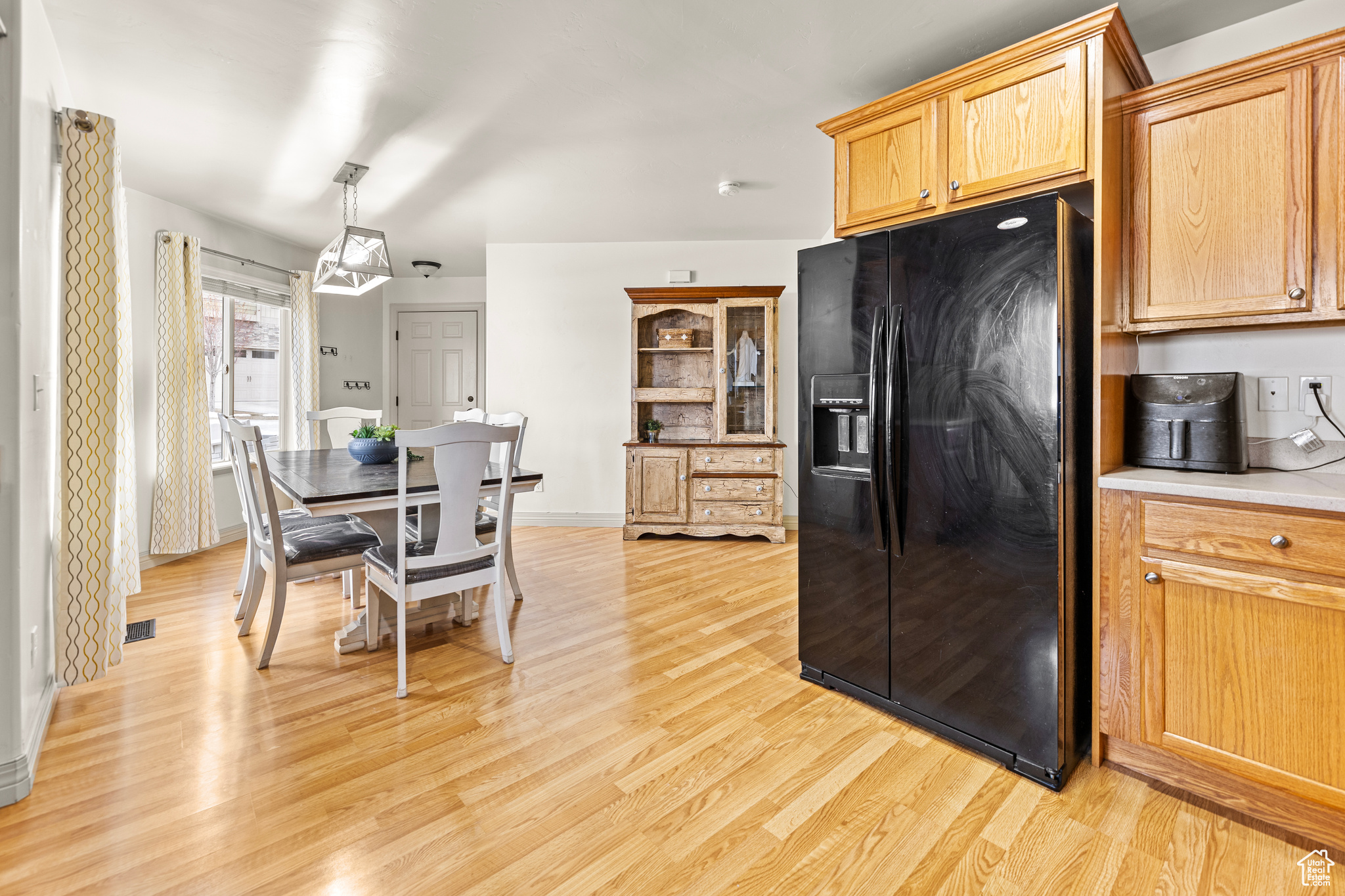 Kitchen with hanging light fixtures, black refrigerator with ice dispenser, light brown cabinets, and light wood-type flooring