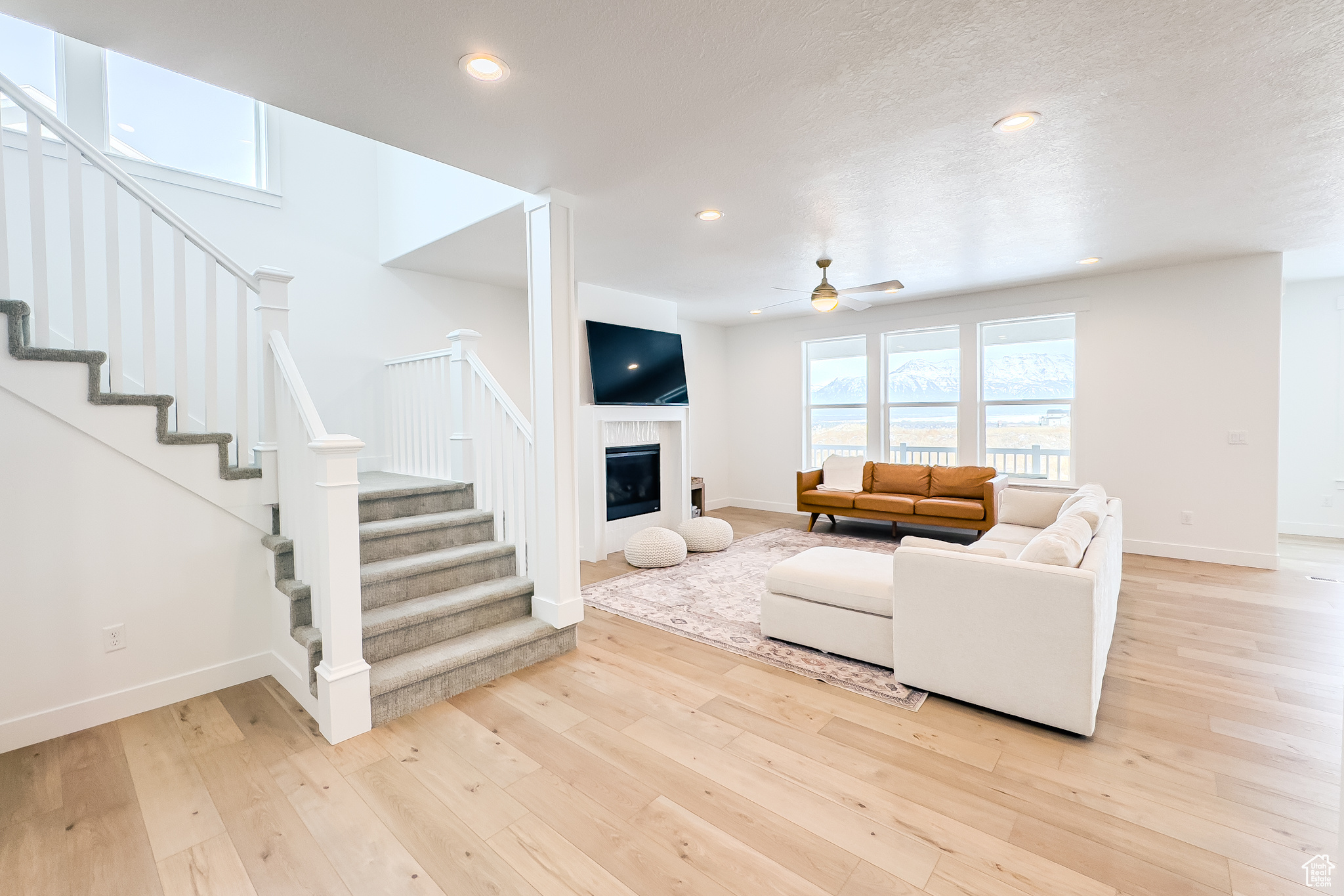 Living room with ceiling fan, a tile fireplace, light hardwood / wood-style flooring, and a textured ceiling