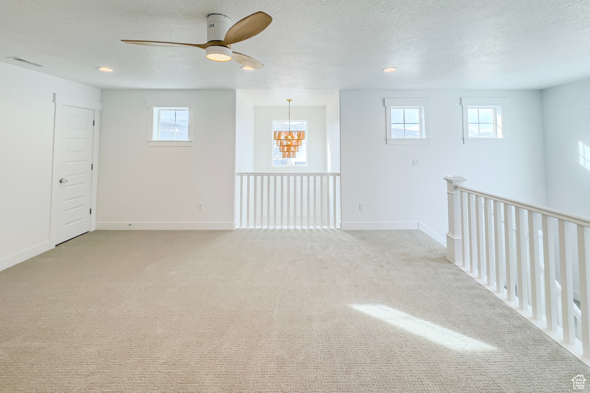 Empty room featuring a wealth of natural light, ceiling fan with notable chandelier, light carpet, and a textured ceiling