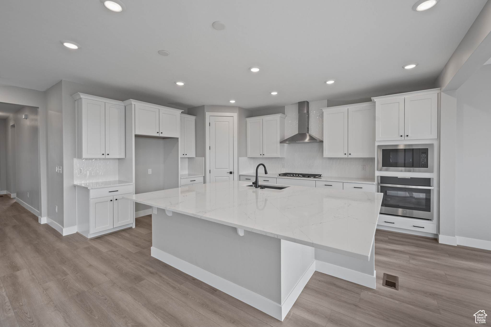 Kitchen featuring a spacious island, sink, wall chimney range hood, oven, and white cabinets