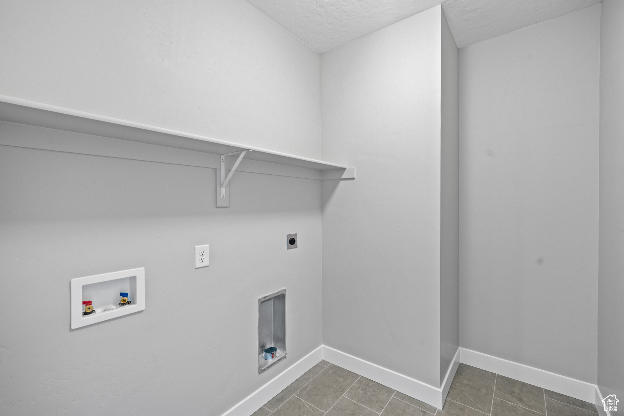 Clothes washing area with tile patterned flooring, hookup for a washing machine, hookup for an electric dryer, and a textured ceiling