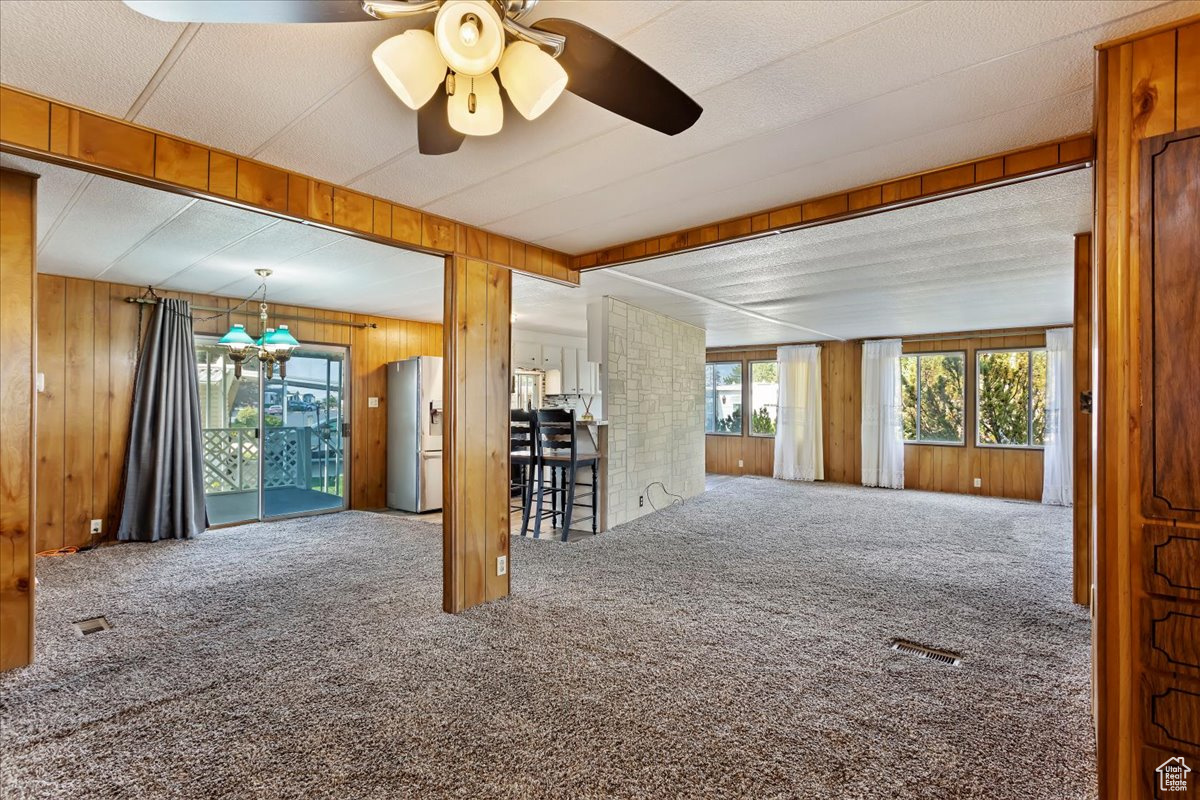 Unfurnished living room with ceiling fan, carpet, and wood walls