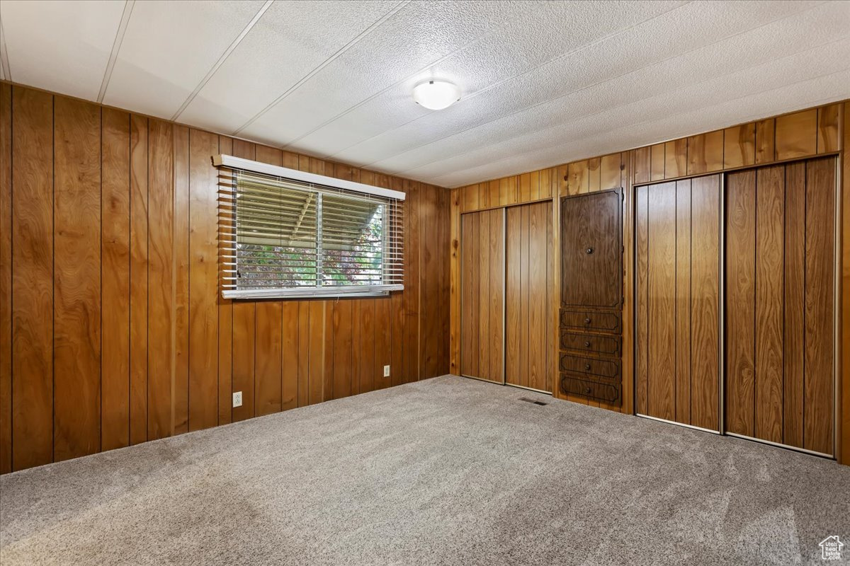 Carpeted empty room featuring a textured ceiling and wood walls