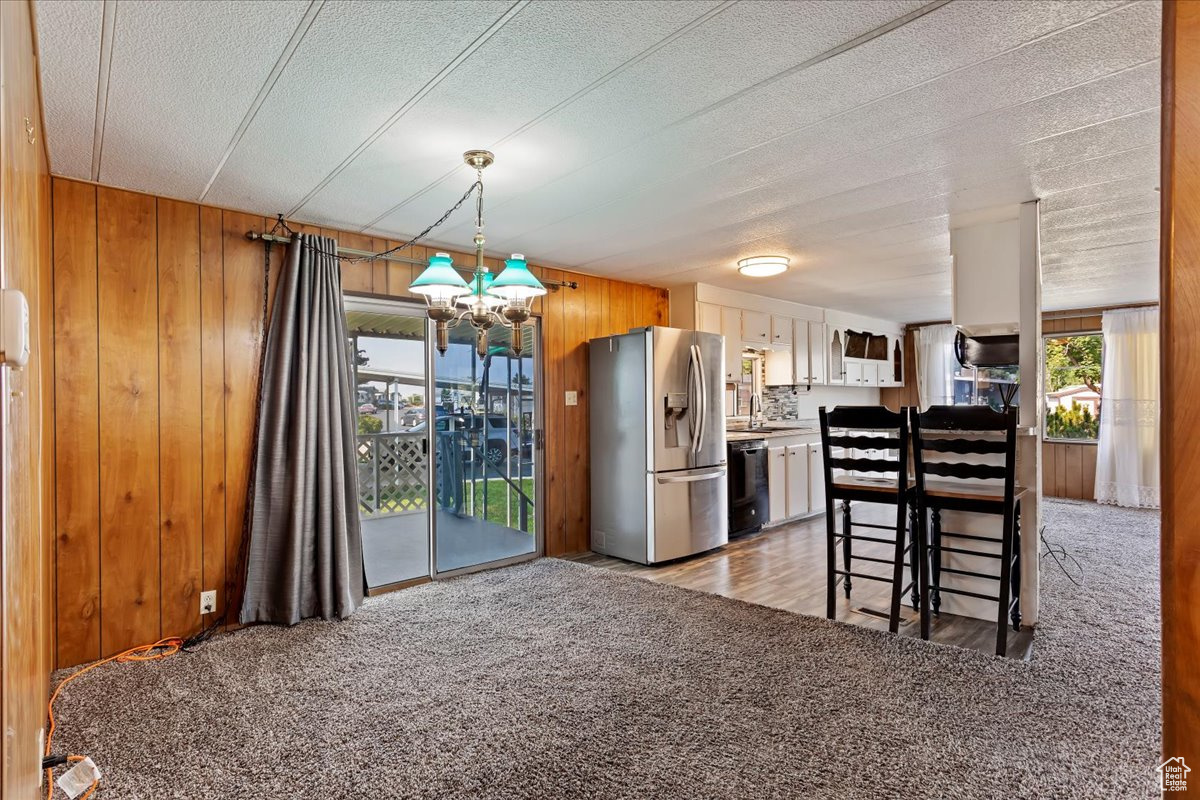 Kitchen with stainless steel fridge with ice dispenser, wooden walls, light colored carpet, and white cabinets