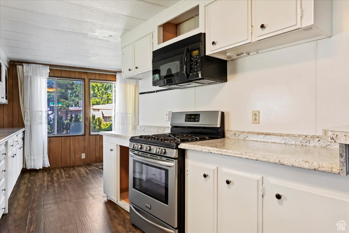 Kitchen with white cabinetry, stainless steel range with gas stovetop, dark hardwood / wood-style flooring, and light stone counters