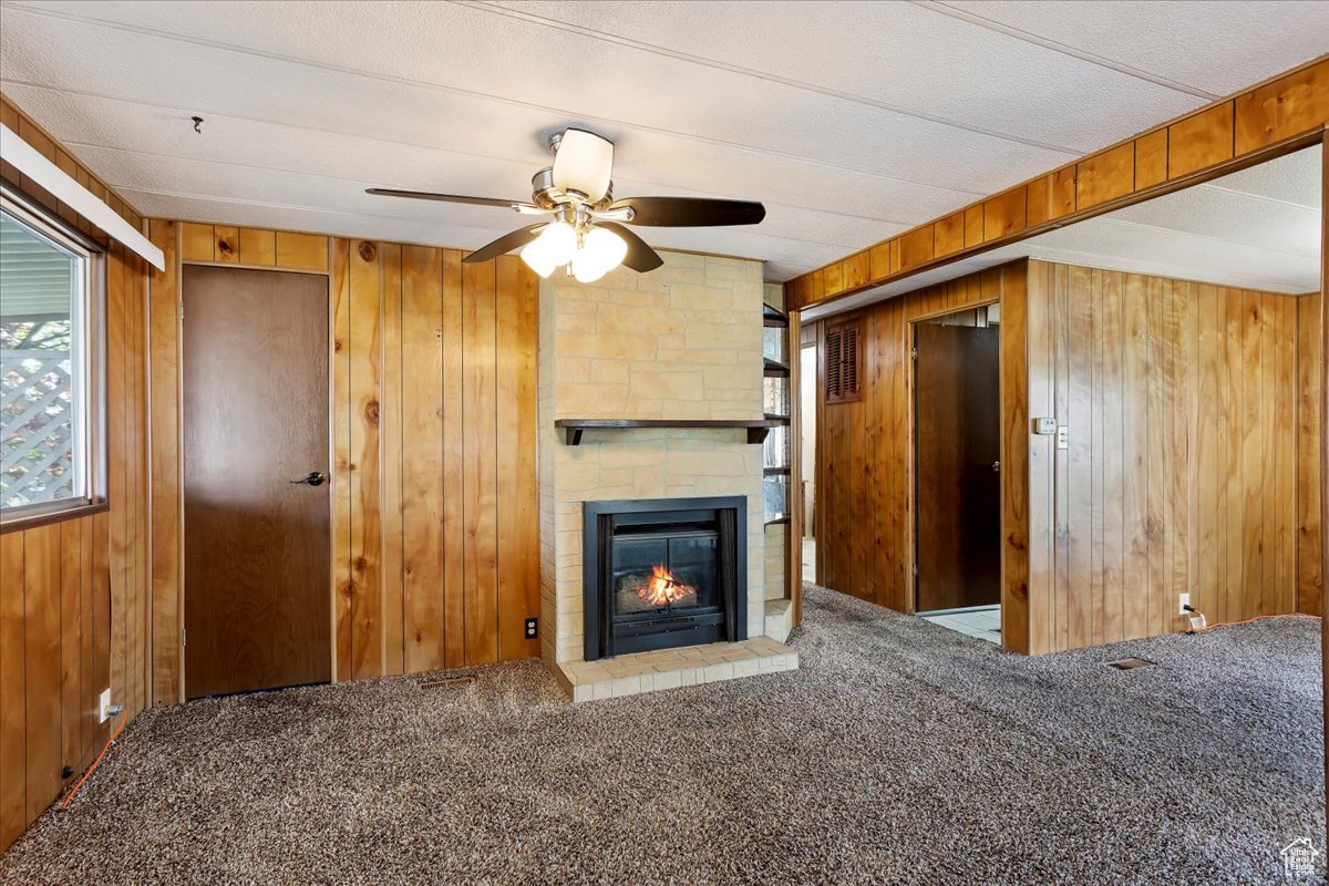 Unfurnished living room with a large fireplace, wooden walls, carpet floors, ceiling fan, and beam ceiling