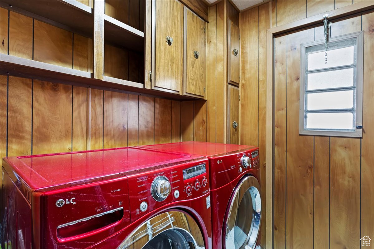 Laundry room with cabinets, separate washer and dryer, and wood walls