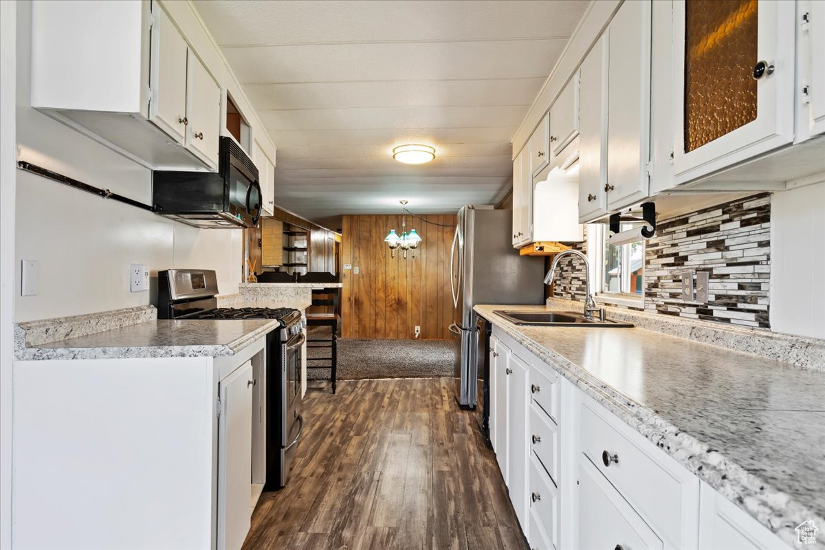 Kitchen with stainless steel gas range, dark hardwood / wood-style floors, pendant lighting, decorative backsplash, and white cabinets