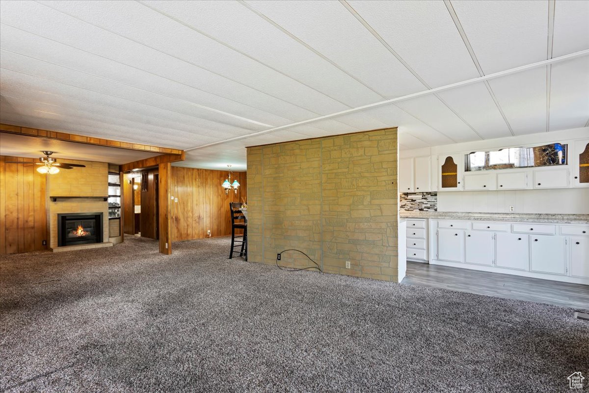 Unfurnished living room featuring wood walls, a chandelier, and dark colored carpet