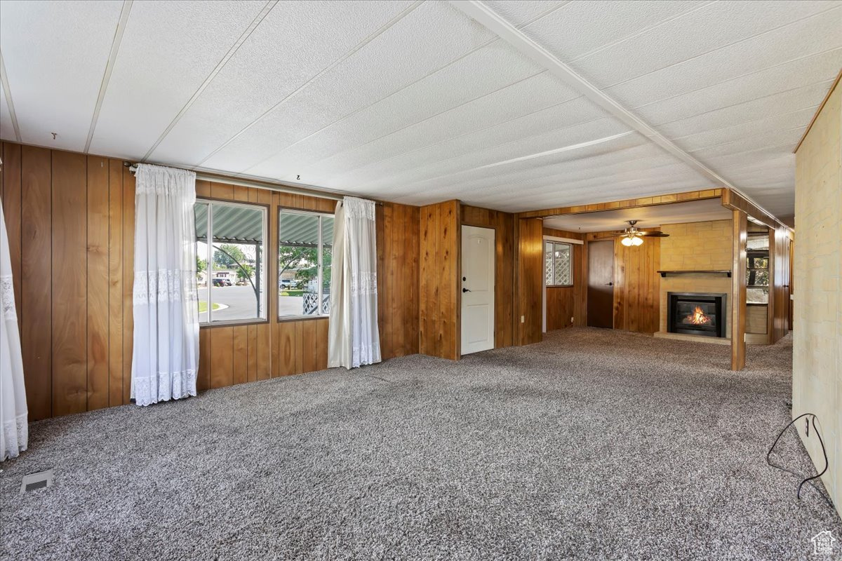 Unfurnished living room featuring ceiling fan, carpet flooring, and wooden walls