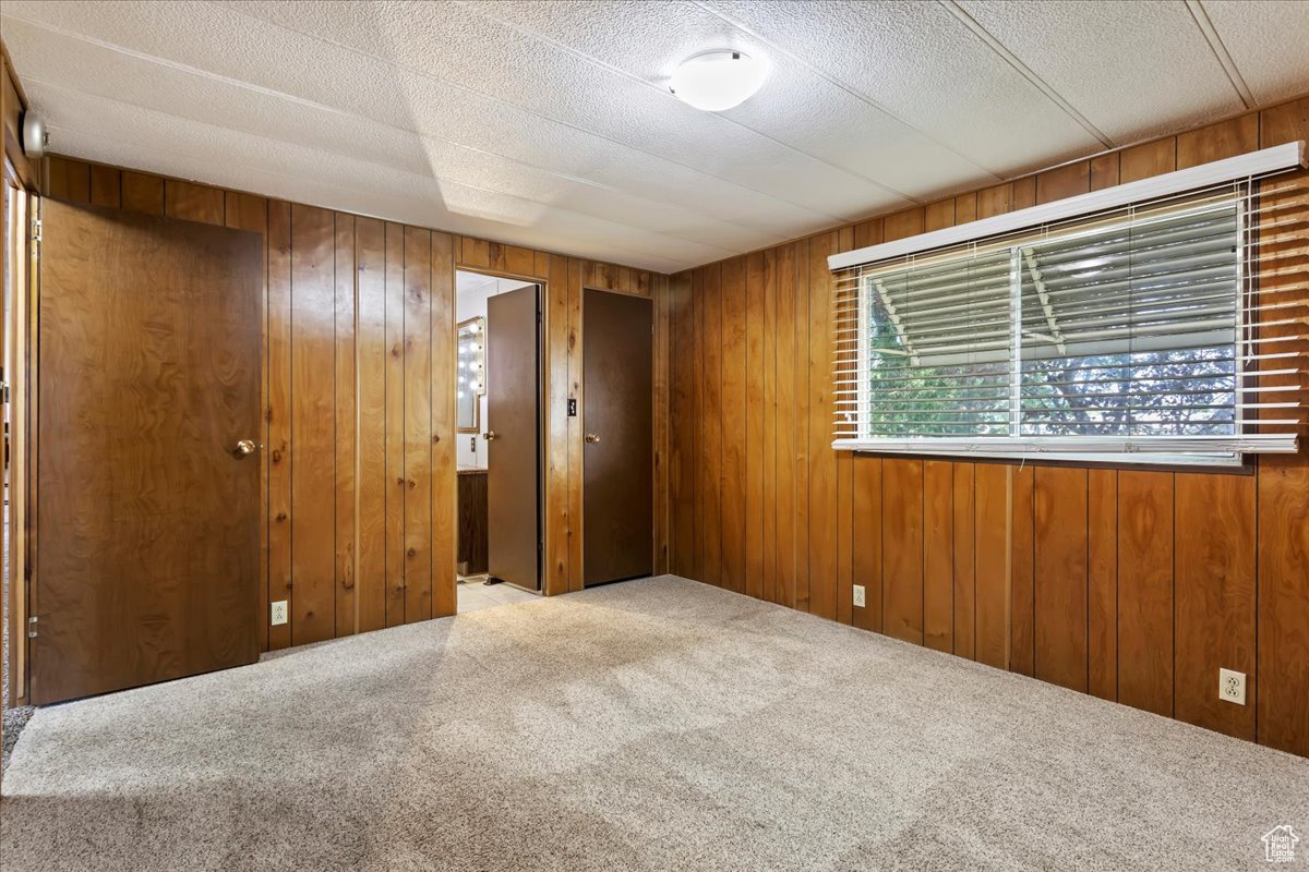 Carpeted empty room featuring wooden walls and a textured ceiling