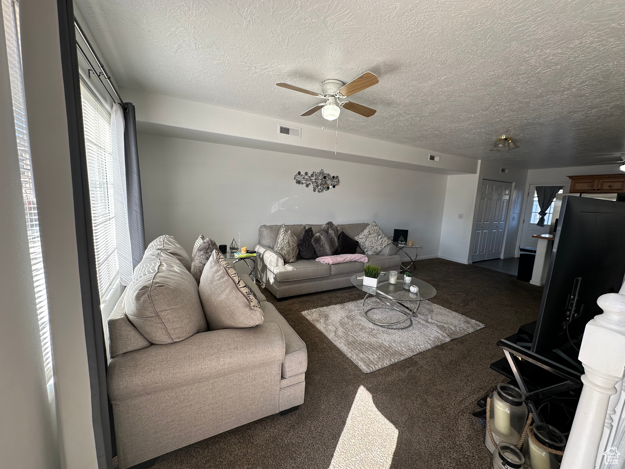 Carpeted living room featuring ceiling fan and a textured ceiling