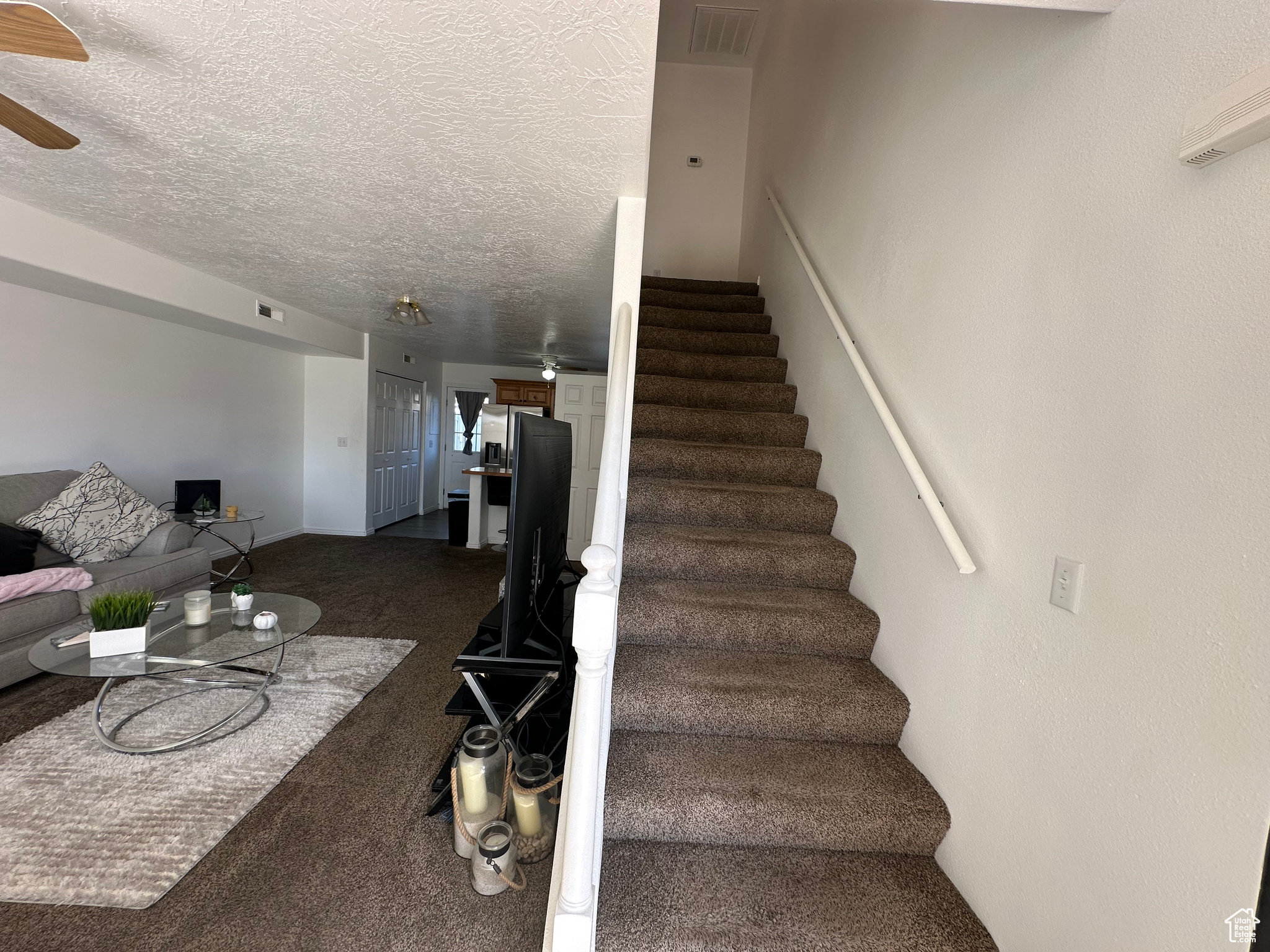 Stairway featuring carpet flooring, a textured ceiling, and ceiling fan