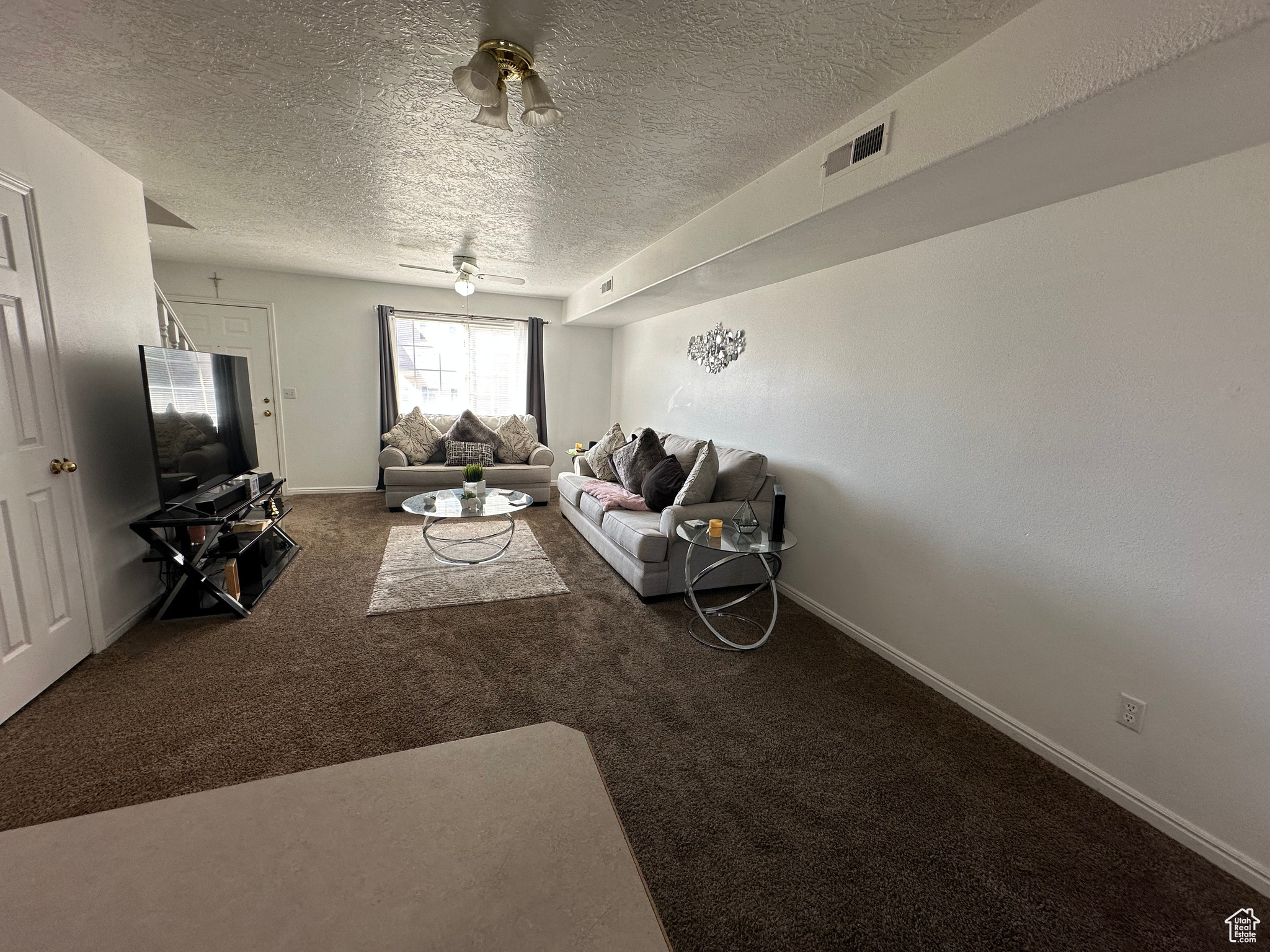 Carpeted living room featuring ceiling fan and a textured ceiling